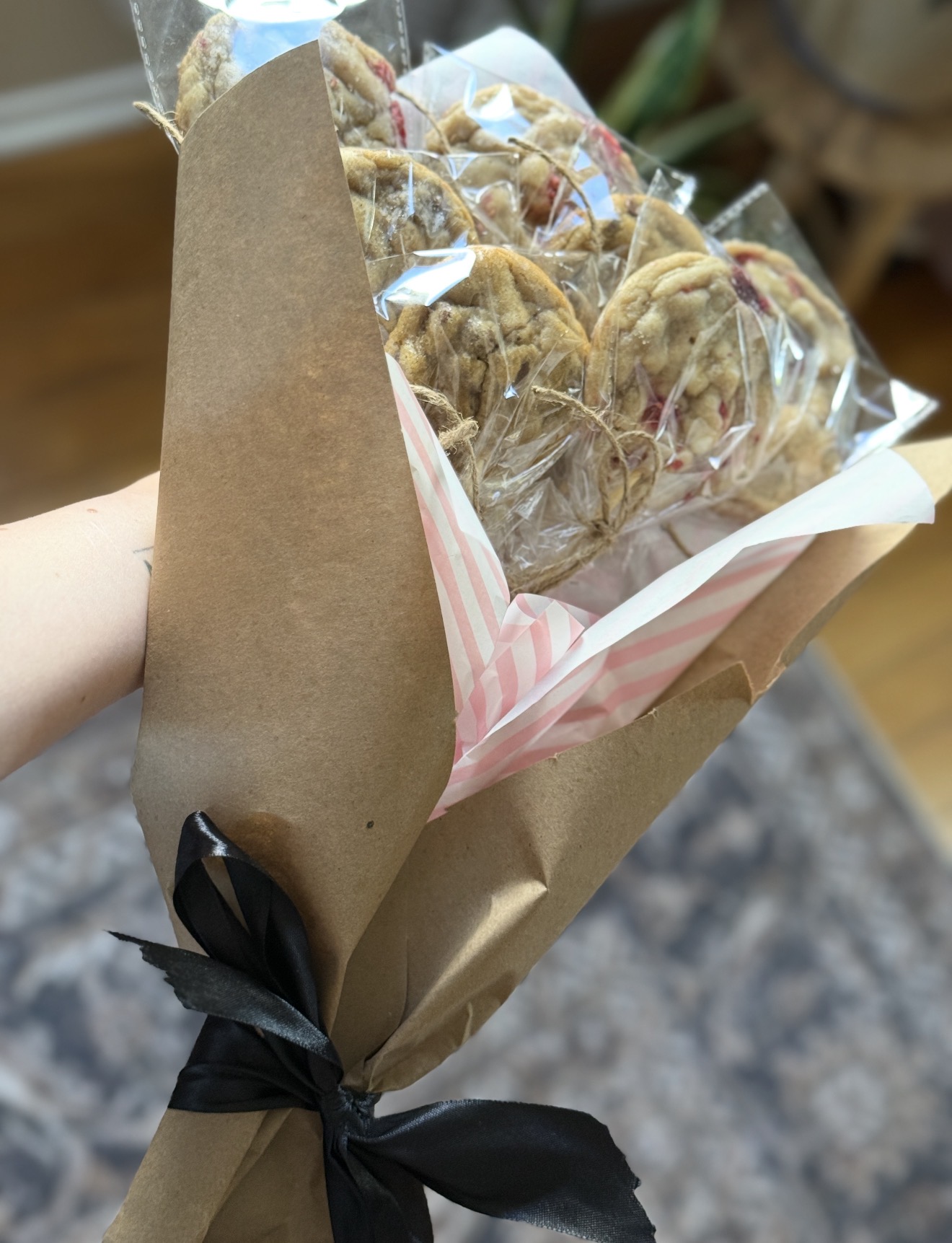A gift-wrapped bouquet of freshly baked cookies, tied with a black ribbon in kraft paper.